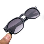 Black square-frame sunglasses with dark lenses held in hand on white background