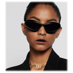 Woman wearing black cat-eye sunglasses with gold trim, gold chain necklace, and black blazer